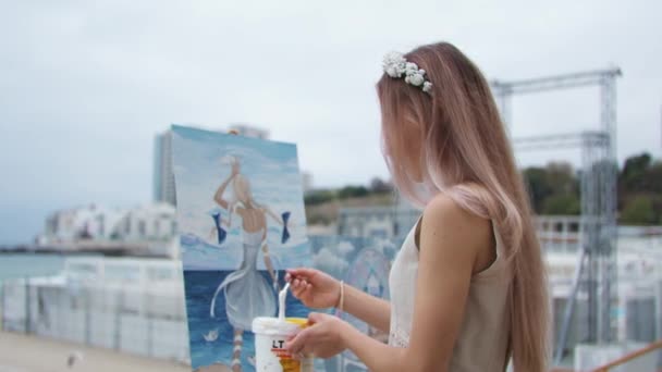Giovane donna bionda dipinge un quadro sulla spiaggia della città all'aria aperta — Video Stock
