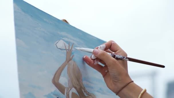 En ung blondine tegner et bilde på stranden i det fri. – stockvideo