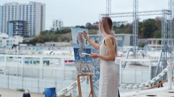 Jong blond vrouw schetst een beeld op de stad strand op open lucht — Stockvideo