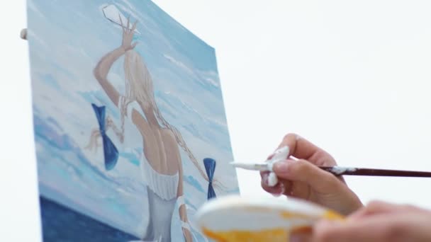 Νεαρή ξανθιά ζωγραφίζει μια εικόνα στην παραλία της πόλης — Αρχείο Βίντεο