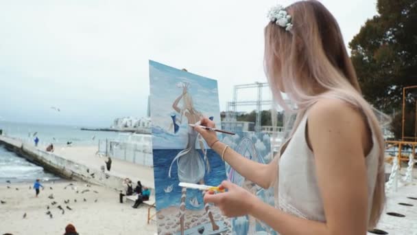 Fiatal szőke nő fest egy képet a város strandján a szabadban — Stock videók