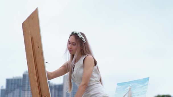 Mladá blond žena maluje obrázek na pláži na čerstvém vzduchu na pozadí létajících racků — Stock video