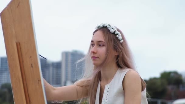 Jonge blonde vrouw schildert beeld op het strand op open lucht tegen de achtergrond van vliegende meeuwen — Stockvideo