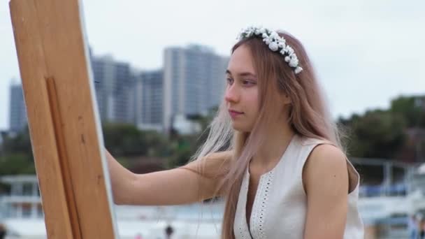 Giovane donna bionda dipinge quadro sulla spiaggia all'aperto Sullo sfondo di gabbiani volanti — Video Stock