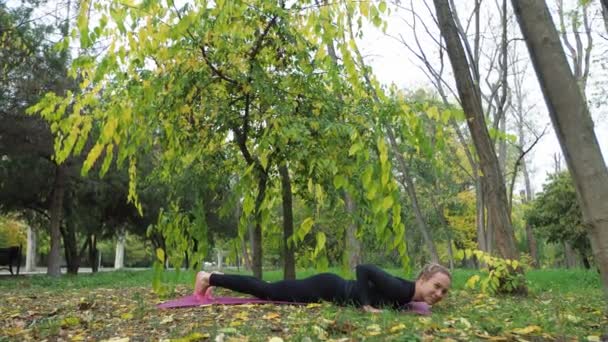 Mujer joven practica yoga en un parque de la ciudad En la hierba — Vídeos de Stock
