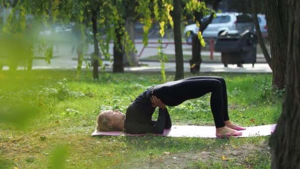 Mujer joven practica yoga en un parque de la ciudad En la hierba — Vídeos de Stock