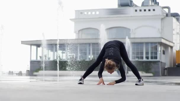 Молодая женщина практикует йогу в городском парке на фоне фонтана — стоковое видео