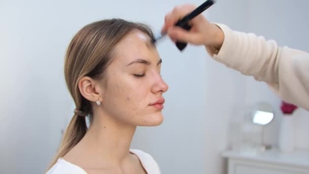 Young brunette woman make-up artist paints a blonde girl in a beauty salon Applies toning cream Acne — Stock Video