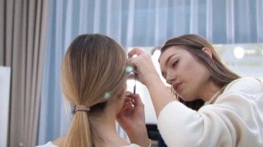 Genç esmer kadın makyaj sanatçısı. Güzellik salonunda sarışın bir kız resmediyor. Göz çevresini boyuyor.