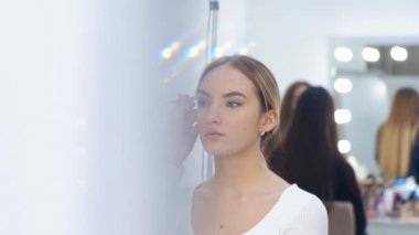 Genç esmer kadın makyaj sanatçısı bir sarışın kızı güzellik salonunda resmediyor.