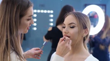 Genç esmer kadın makyaj sanatçısı sarışın bir kızı güzellik salonunda boyuyor dudaklarını boyuyor.