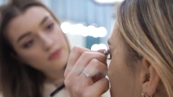 Young brunette woman make-up artist paints a blonde girl in a beauty salon Eyeshadows — Stock Video