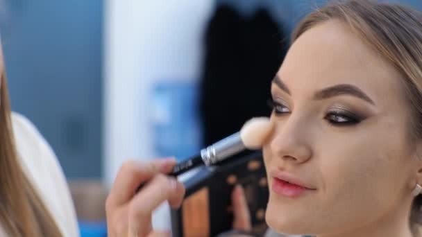 Joven morena maquilladora pinta a una chica rubia en un salón de belleza Eyeshadows — Vídeo de stock