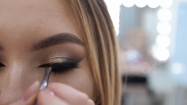 Ung brunett kvinna make-up artist målar en blond flicka i en skönhetssalong Målar ögonen — Stockvideo