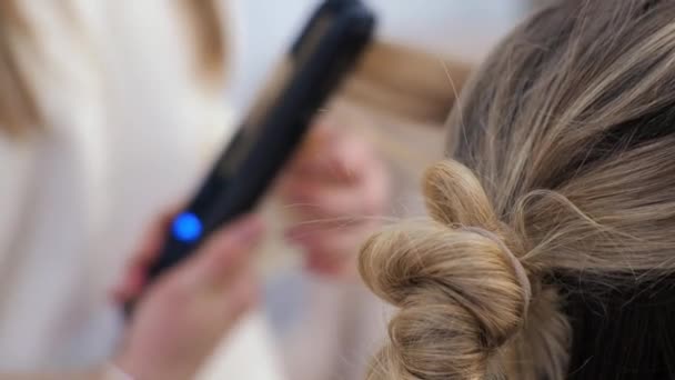 Junge brünette Frau Friseur macht Styling auf den langen Haaren des blonden Mädchens — Stockvideo