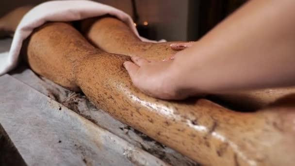 Vrouw masseur maakt schrobben massage van de benen koffie pomace massage op een donkere warme achtergrond — Stockvideo