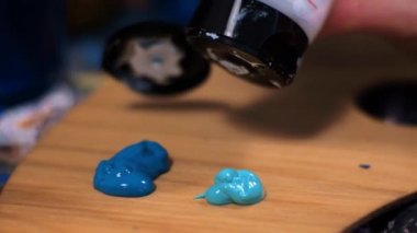 Genç kadın sanatçı bir palete akrilik boya sıkıyor.