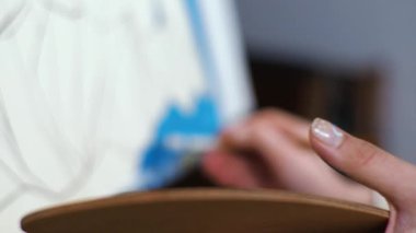 Genç sarışın kadın ressam mavi renkli makro paletle bir resim çiziyor.