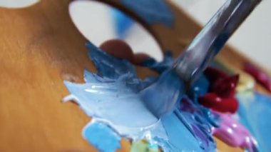 Genç sarışın kadın ressam mavi renkli makro paletle bir resim çiziyor.