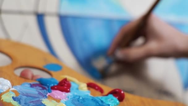 Joven artista rubia pinta un cuadro en colores azules Paleta de Primer plano — Vídeos de Stock