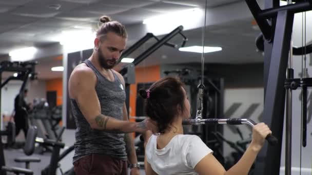 Gym Lesson egy fiatal vicces edző férfi Egy kezdő nő rázza a hátát és a karját a szimulátor — Stock videók