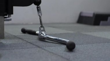 Genç adam spor salonunda çalışıyor. Ciddi şekilde odaklanmış. Kolların bisepslerini simülatöre doğru sallıyor.