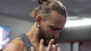 Genç adam spor salonunda çalışıyor. Ciddi şekilde odaklanmış. Kolların bisepslerini simülatöre doğru sallıyor.