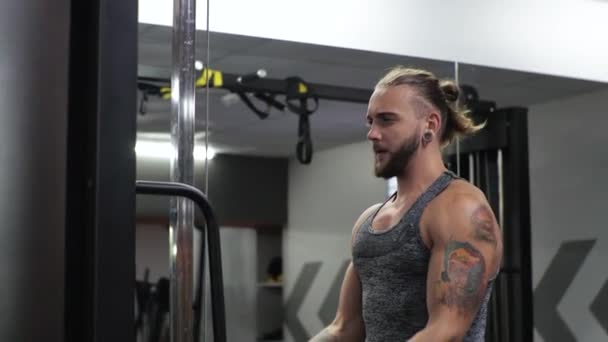O jovem trabalha no ginásio. Sério focado balança o bíceps dos braços no simulador — Vídeo de Stock