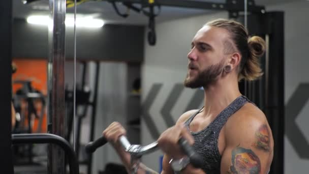 El joven trabaja en el gimnasio. Enfoque serio Mueve el bíceps de los brazos en el simulador — Vídeos de Stock