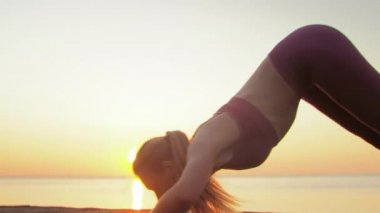 Kumsalda yoga yapan genç sarışın kadın güneşin doğuşunun ya da batışının arka planında