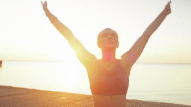 Kumsalda yoga yapan genç sarışın kadın güneşin doğuşunun ya da batışının arka planında