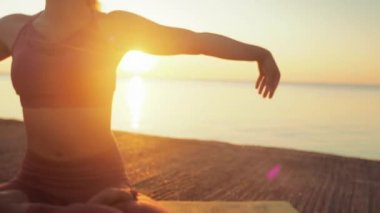 Kumsalda yoga yapan genç sarışın kadın güneşin doğuşunun ya da batışının arka planında