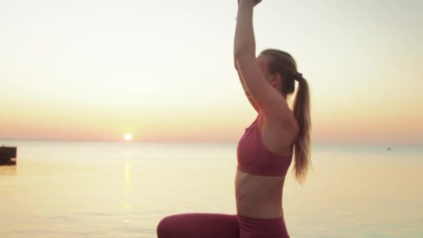 Młoda blondynka zaangażowana w jogę na plaży przy morzu tle wschodu lub zachodu słońca — Wideo stockowe