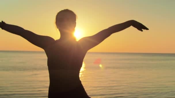 Giovane donna bionda impegnata in yoga sulla spiaggia sullo sfondo del mare dell'alba o del tramonto — Video Stock