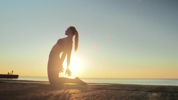 Jovem mulher loira envolvida em ioga na praia pelo fundo do mar do nascer ou pôr do sol — Vídeo de Stock