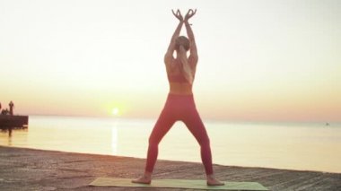 Kumsalda yoga yapan genç sarışın kadın güneşin doğuşunun ya da batışının arka planında