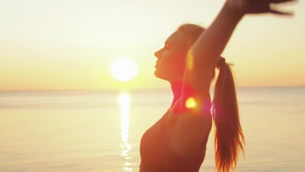 Wanita muda berambut pirang melakukan yoga di pantai dengan latar belakang laut matahari terbit atau terbenam — Stok Video