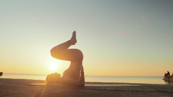 Kumsalda yoga yapan genç sarışın kadın güneşin doğuşunun ya da batışının arka planında — Stok video