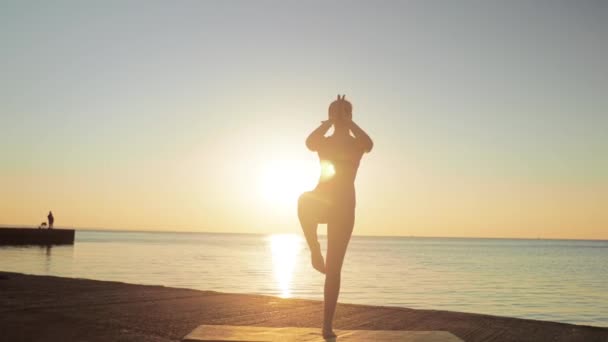 Young blonde woman engaged in yoga on the beach by the sea background of the sunrise or sunset — Stock Video