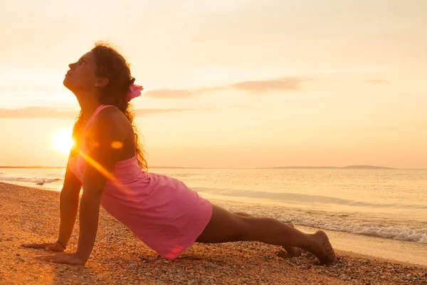 Fiatal lány a strandon, napkeltekor csinálás jóga gyakorlás — Stock Fotó
