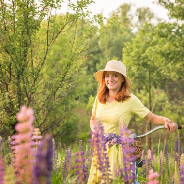 Çiçekli çayırda bisiklet süren genç bir kız.