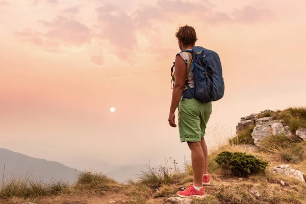 Jeden turysta z plecakami cieszący się zachodem słońca na szczycie góry — Zdjęcie stockowe