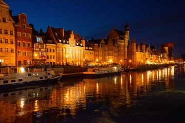 Gdansk nehir kenarındaki gece gösterileri Motlawa Nehri 'ni yansıtan tarihi binalar güzel aydınlatılıyor. İnsanlar gezinti güvertesinde, huzurlu bir akşam atmosferinin tadını çıkarıyorlar.