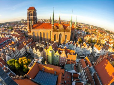 Gdansk 'taki tarihi St. Marys Kilisesi' nin sıcak güneş ışığı altında renkli çatılarla çevrili havadan görüntüsü. Sahne şehrin mimari güzelliğini ve kültürel zenginliğini vurguluyor.