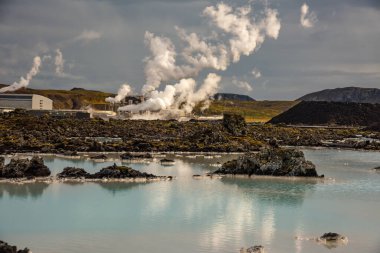 İzlanda 'daki Blue Lagoon' un grevdeki arka planına karşı bir jeotermal enerji santrali kuruldu. Tesisten buhar yükseliyor ve ön plandaki turkuaz sularda su birikiyor..