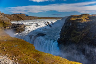 İzlanda 'daki Gullfoss şelalesi kanyona akan güçlü çağlayanları gösteriyor. Ziyaretçiler, yakınlardaki doğal güzelliklere özellikle güneşli havalarda hayranlık duyarlar..