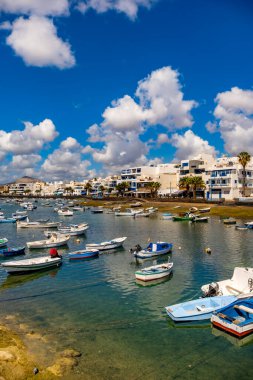 Lanzarote 'deki Arrecife Lagoon' un canlı bir sahnesinde sayısız tekne berrak sularda huzur içinde yüzüyor. Modern binalar ve uzak dağlar sakin arkaplanı tamamlıyor