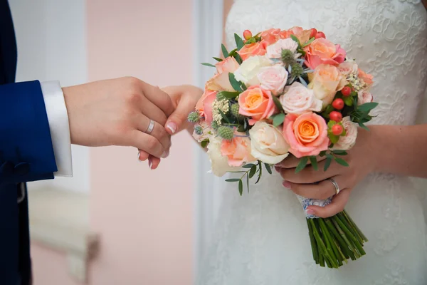 Mãos da noiva e do noivo no fundo de um closeup do buquê de casamento — Fotografia de Stock