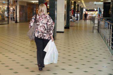 Alışverişi olan kadın alışveriş merkezinde, arka planda yürüyor..