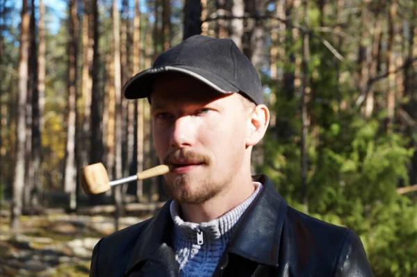 young man in a cap smokes a pipe in the forest, portrait
